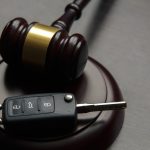Close-up Of Gavel And Car Key On Sounding Block Against Grey Background